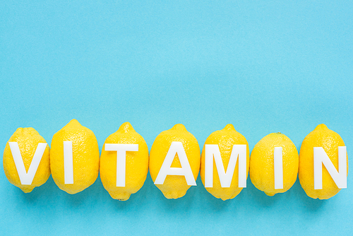 top view of ripe yellow lemons and word vitamin on blue background