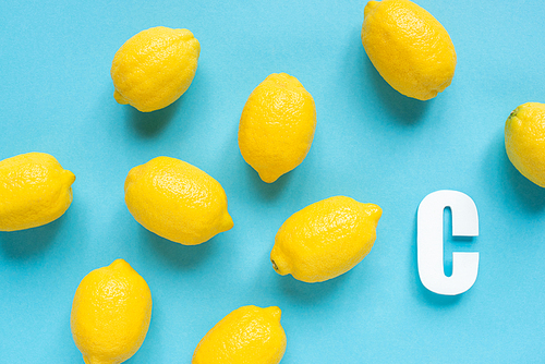 top view of ripe yellow lemons and letter C on blue background