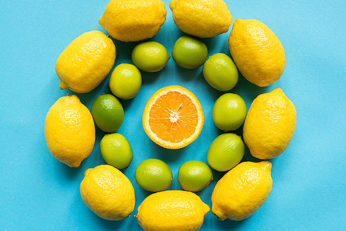 top view of ripe yellow lemons, orange and limes arranged in circles on blue background