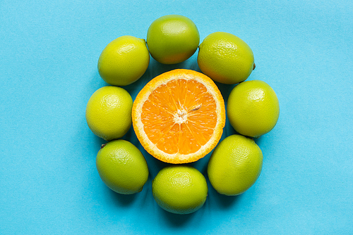 top view of ripe orange and limes arranged in circle on blue background