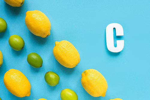 flat lay with ripe yellow lemons, green limes and letter C on blue background