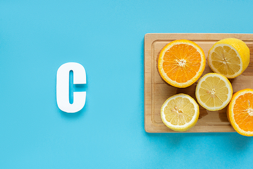 top view of ripe cut lemon and orange on wooden cutting board near letter C on blue background