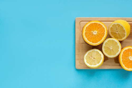 top view of ripe cut lemon and orange on wooden cutting board on blue background