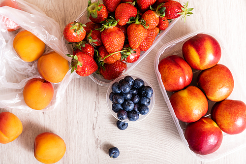 top view of fruit composition with blueberries, strawberries, nectarines and peaches in plastic containers on wooden surface