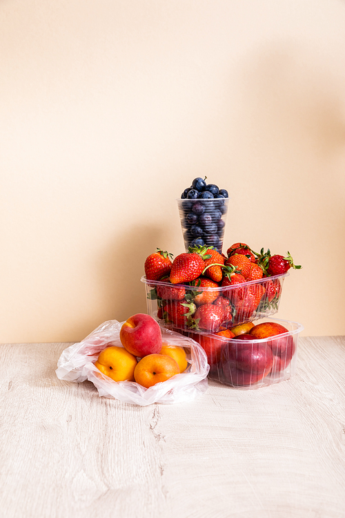 fruit composition with blueberries, strawberries, nectarines and peaches in plastic containers on wooden surface on beige background
