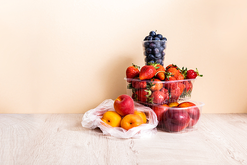 fruit composition with blueberries, strawberries, nectarines and peaches in plastic containers on wooden surface on beige background