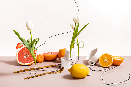 floral and fruit composition with tulips, fruits, cutlery isolated on beige