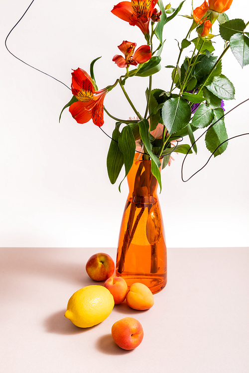 floral composition with roses and red Alstroemeria in wires in orange vase near lemon and apricots isolated on white