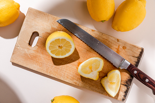 top view of whole and cutted lemons on wooden board with knife on grey table