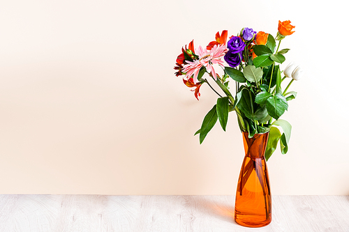 floral composition with bouquet in orange vase on wooden surface on beige background