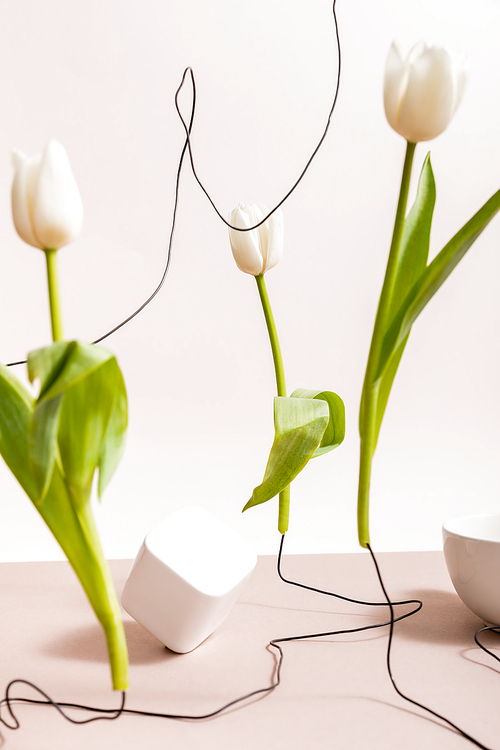 selective focus of creative floral composition with tulips on wires, cup and square cube isolated on beige