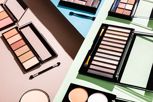 eye shadow and blush palettes near cosmetic brushes on green, blue and pink