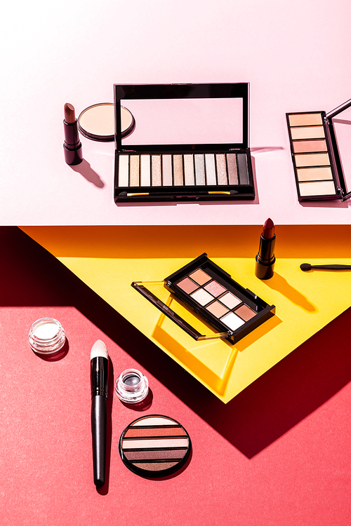 eye shadow palettes near cosmetic brushes, lipsticks and face powder on crimson, pink and yellow