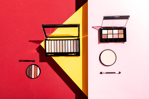 top view of eye shadow palettes and double-sided eyeshadow applicators near face powder on crimson, pink and yellow