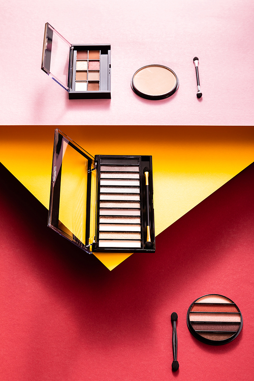 eye shadow palettes and double-sided eyeshadow applicators near face powder on crimson, pink and yellow