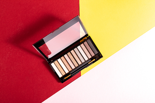 top view of eye shadow palette and double-sided eyeshadow brush on crimson, pink and yellow
