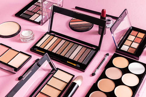 blush and eye shadow palettes near cosmetic brushes and lipstick on pink