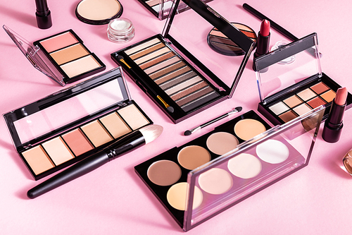 blush and eye shadow palettes near cosmetic brushes and lipsticks on pink