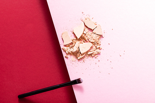 top view of cracked face powder and cosmetic brush on crimson and pink