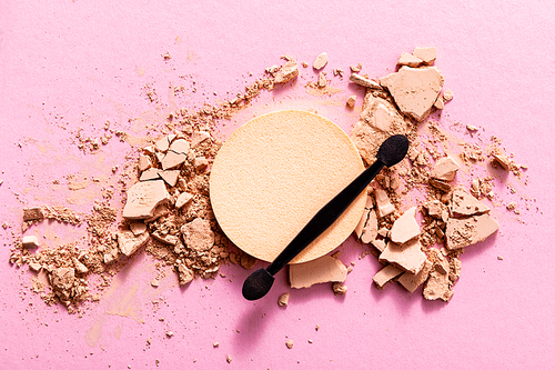 top view of double-sided eyeshadow applicator near cracked face powder and makeup sponge on pink