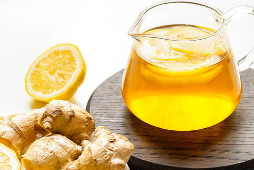 hot tea in teapot on wooden board near ginger root, lemon on white background