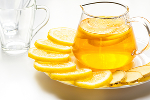 hot tea in glass teapot with lemon slices and ginger on white background