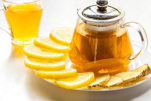selective focus of hot tea in glass teapot with lemon slices and ginger and cup on white background