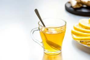 selective focus of hot tea in glass cup with spoon near lemon slices on white background