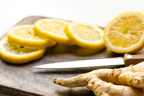 selective focus of hot ginger root, lemon on wooden cutting board with knife on white background