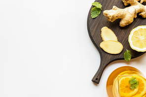 top view of hot tea in teapot served near wooden board with ginger root, lemon and mint on white background