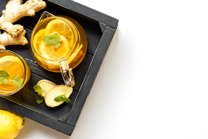 top view of hot tea with ginger root, lemon and mint on wooden tray on white background
