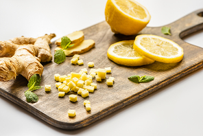 selective focus of ginger root, lemon and mint on wooden cutting board on white background
