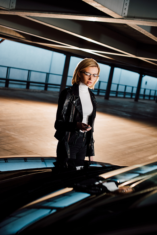 attractive young woman in glasses standing in parking near black car