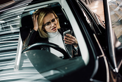 emotional girl in glasses looking at smartphone in car