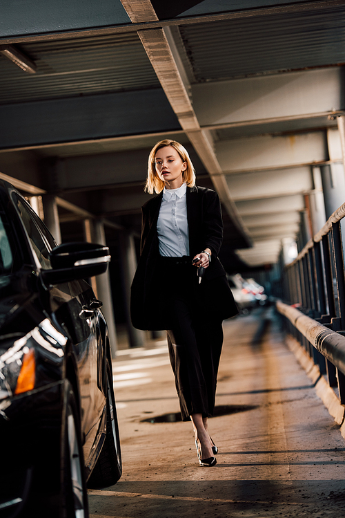 attractive blonde woman walking near black automobile in parking