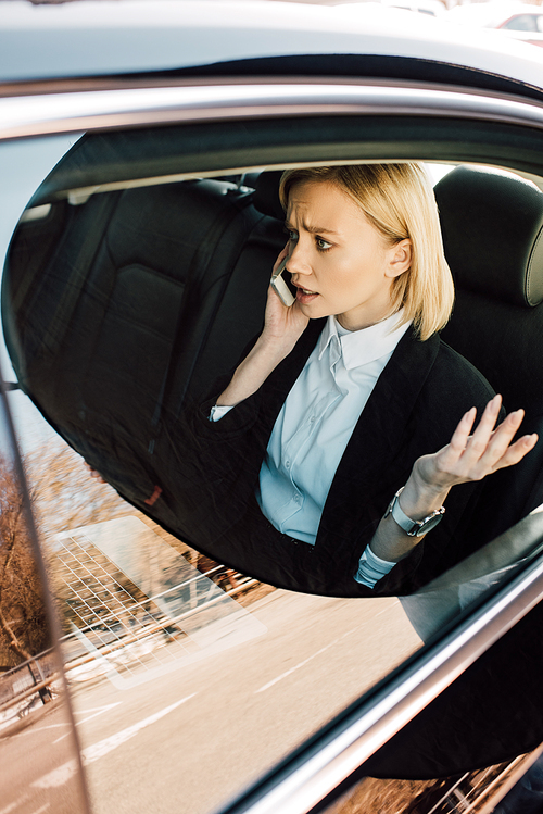 overhead view of upset blonde woman talking on smartphone and gesturing in car