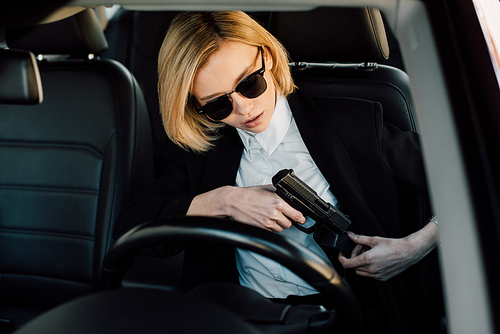 dangerous blonde woman in sunglasses holding gun in car