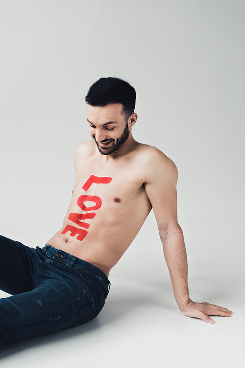 Smiling shirtless man with inscription on body sitting on grey