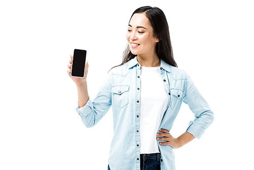 attractive and smiling asian woman in denim shirt holding smartphone with copy space isolated on white