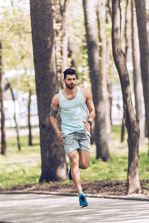 handsome man in sportswear running along pavement in park