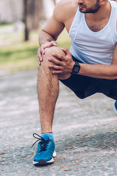 cropped shot of man in sportswear touching injured knee