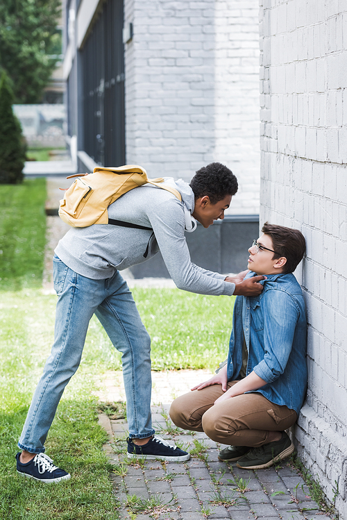 aggressive and brunette african american boy bulling scared boy in glasses