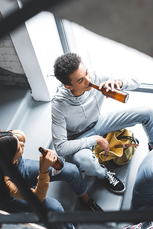 high angle view of teenagers talking, sitting on stairs and drinking beer