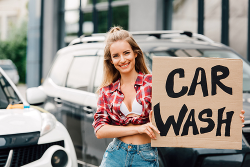 happy girl holding carton board with car wash lettering near cars