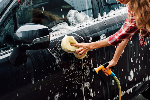cropped view of young woman washing wet car in foam with sponge