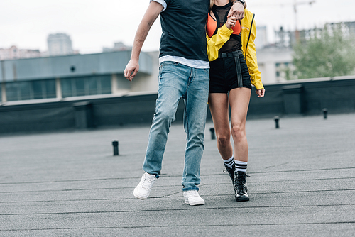 cropped view of man in t-shirt and jeans and woman in yellow jacket hugging on roof