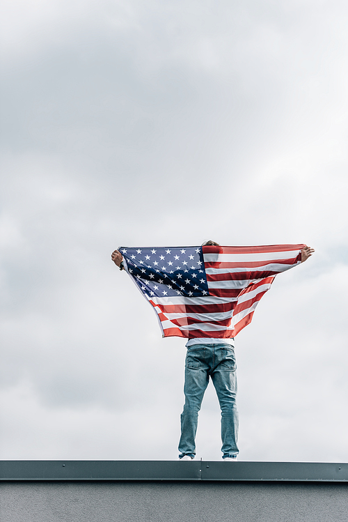 back view of man in jeans holding american flag on roof