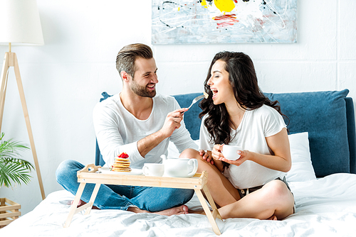 happy man feeding woman with cup in bed at morning