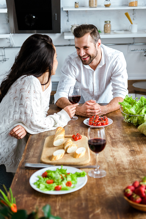 young couple drinking red wine at wooden table with cherry tomatoes, bread and salad