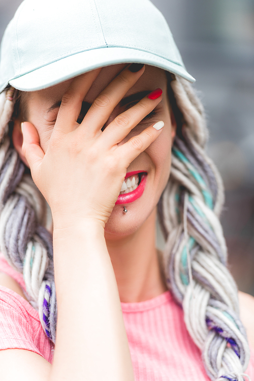 girl with dreadlocks in hat laughing and covering face